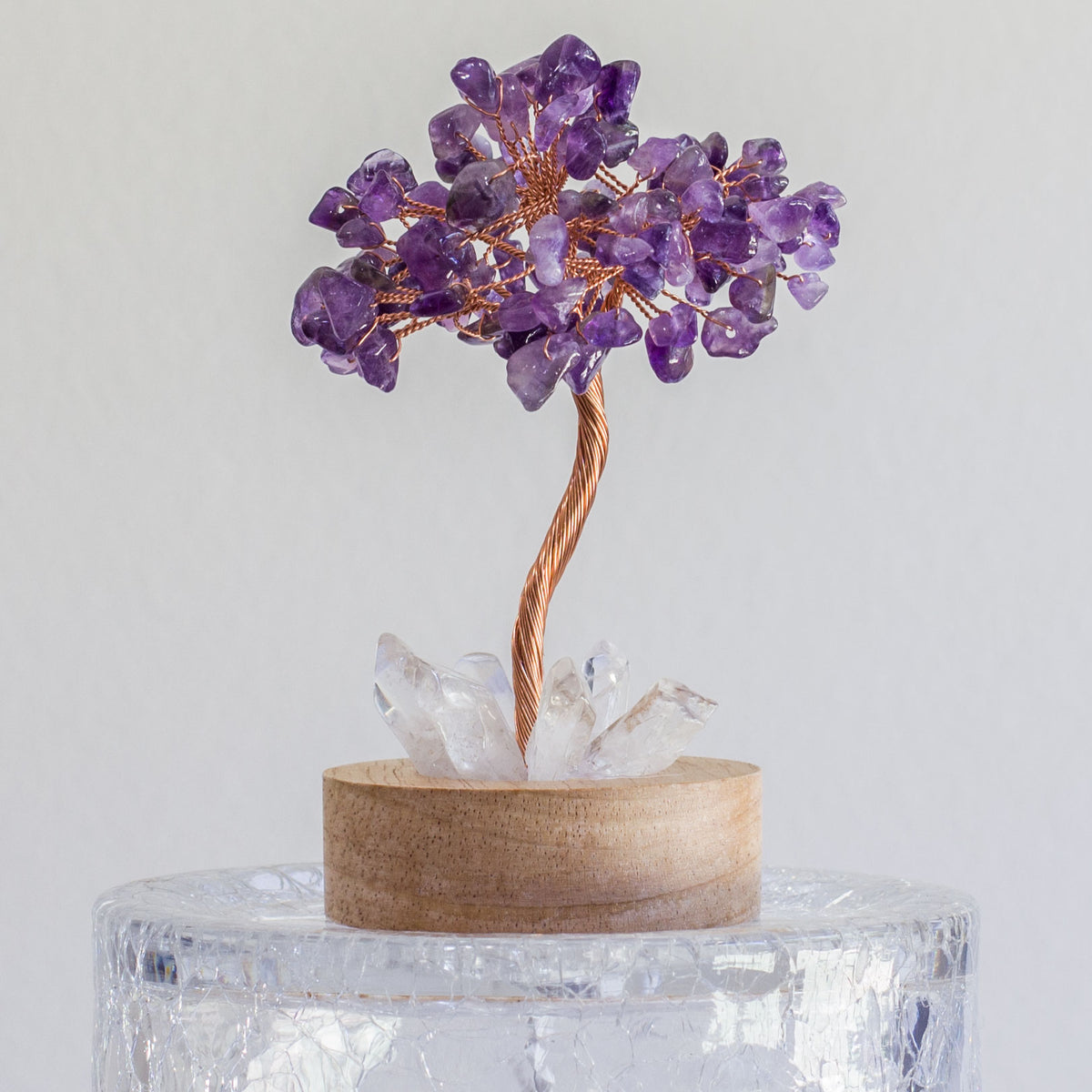 Indulge in a peaceful night&#39;s sleep next to a stunning crystal tree of life, carefully crafted to promote energetic healing and a serene ambiance. Immerse yourself in the gentle, calming glow emanating from the precisely cut clear quartz points, arranged meticulously on a natural, visually appealing wooden base. Accentuating the entire structure is a delicate copper wire stem, elegantly adorned with your choice of crystal chip leaf topping.