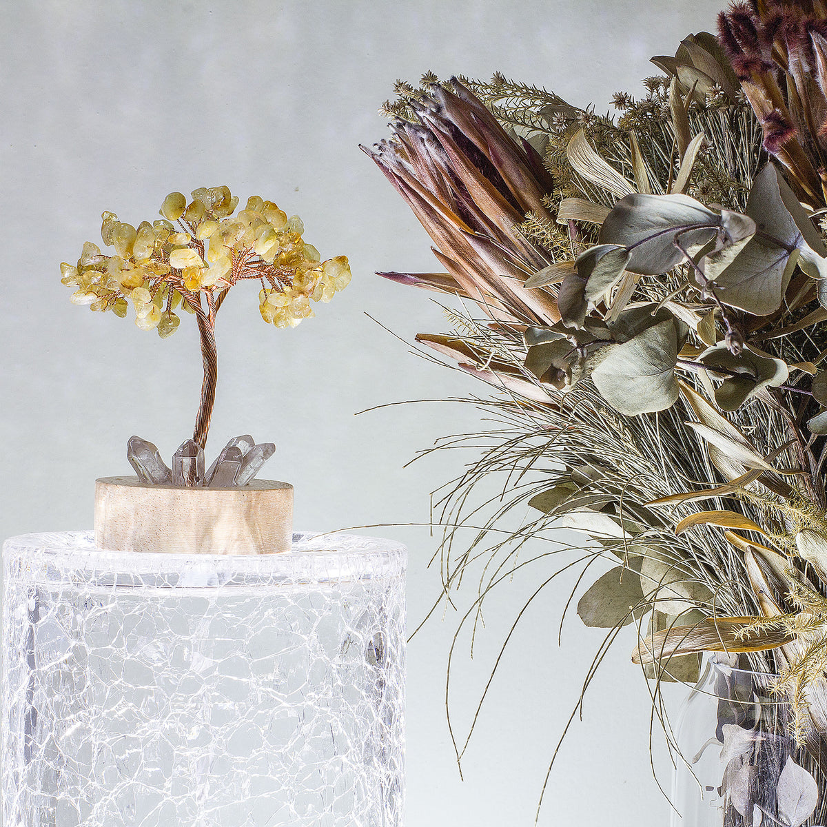 Indulge in a peaceful night&#39;s sleep next to a stunning crystal tree of life, carefully crafted to promote energetic healing and a serene ambiance. Immerse yourself in the gentle, calming glow emanating from the precisely cut clear quartz points, arranged meticulously on a natural, visually appealing wooden base. Accentuating the entire structure is a delicate copper wire stem, elegantly adorned with your choice of crystal chip leaf topping.