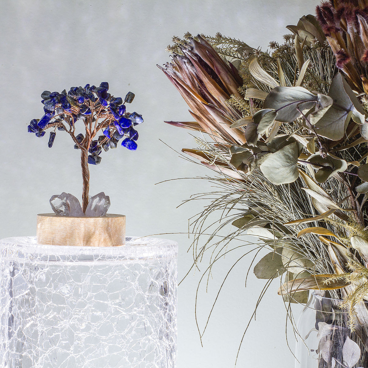 Indulge in a peaceful night&#39;s sleep next to a stunning crystal tree of life, carefully crafted to promote energetic healing and a serene ambiance. Immerse yourself in the gentle, calming glow emanating from the precisely cut clear quartz points, arranged meticulously on a natural, visually appealing wooden base. Accentuating the entire structure is a delicate copper wire stem, elegantly adorned with your choice of crystal chip leaf topping.