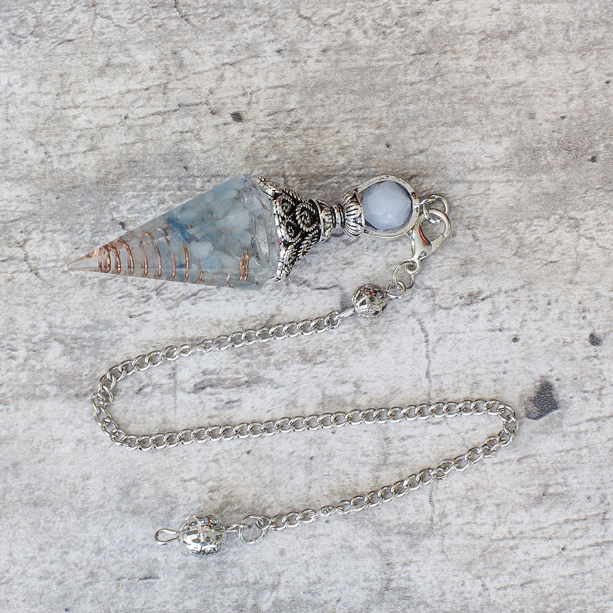 Pendulum - Aquamarine - Resin Mi Chakra - A crystal pendulum is a simple tool commonly used for divination and dowsing. It typically consists of a crystal or gemstone suspended on a chain or cord. The crystal is usually pointed, allowing it to swing freely and respond to questions. Pendulums are believed to connect with your subconscious mind and energy fields, offering insights through their movements.