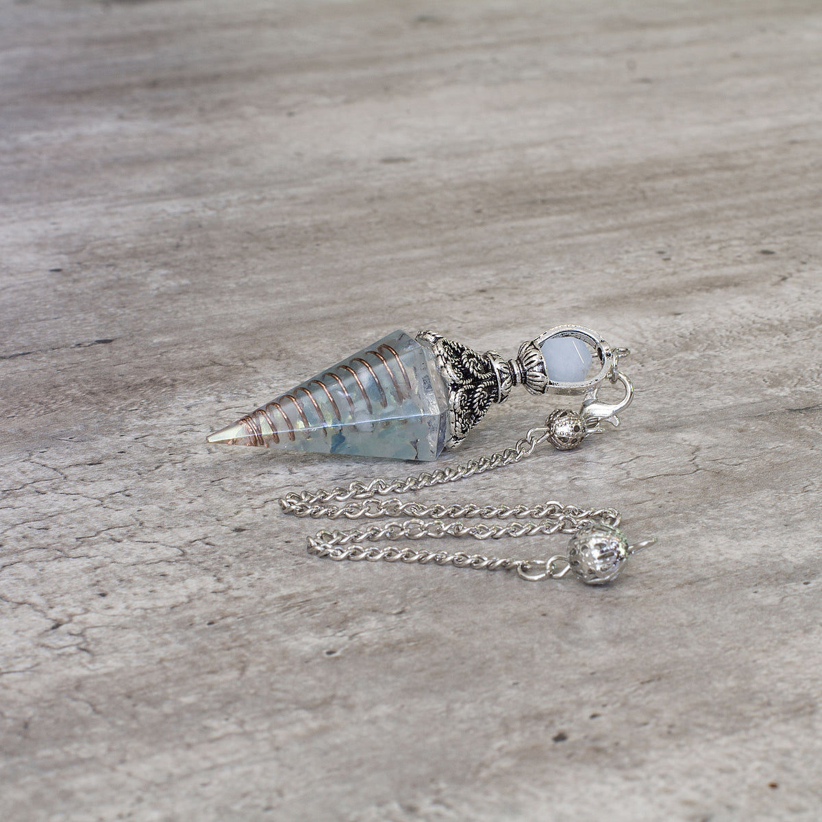 Pendulum - Aquamarine - Resin Mi Chakra - A crystal pendulum is a simple tool commonly used for divination and dowsing. It typically consists of a crystal or gemstone suspended on a chain or cord. The crystal is usually pointed, allowing it to swing freely and respond to questions. Pendulums are believed to connect with your subconscious mind and energy fields, offering insights through their movements.