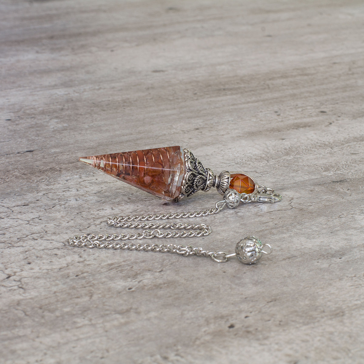 Pendulum - Carnelian - Resin Mi Chakra - A crystal pendulum is a simple tool commonly used for divination and dowsing. It typically consists of a crystal or gemstone suspended on a chain or cord. The crystal is usually pointed, allowing it to swing freely and respond to questions. Pendulums are believed to connect with your subconscious mind and energy fields, offering insights through their movements.
