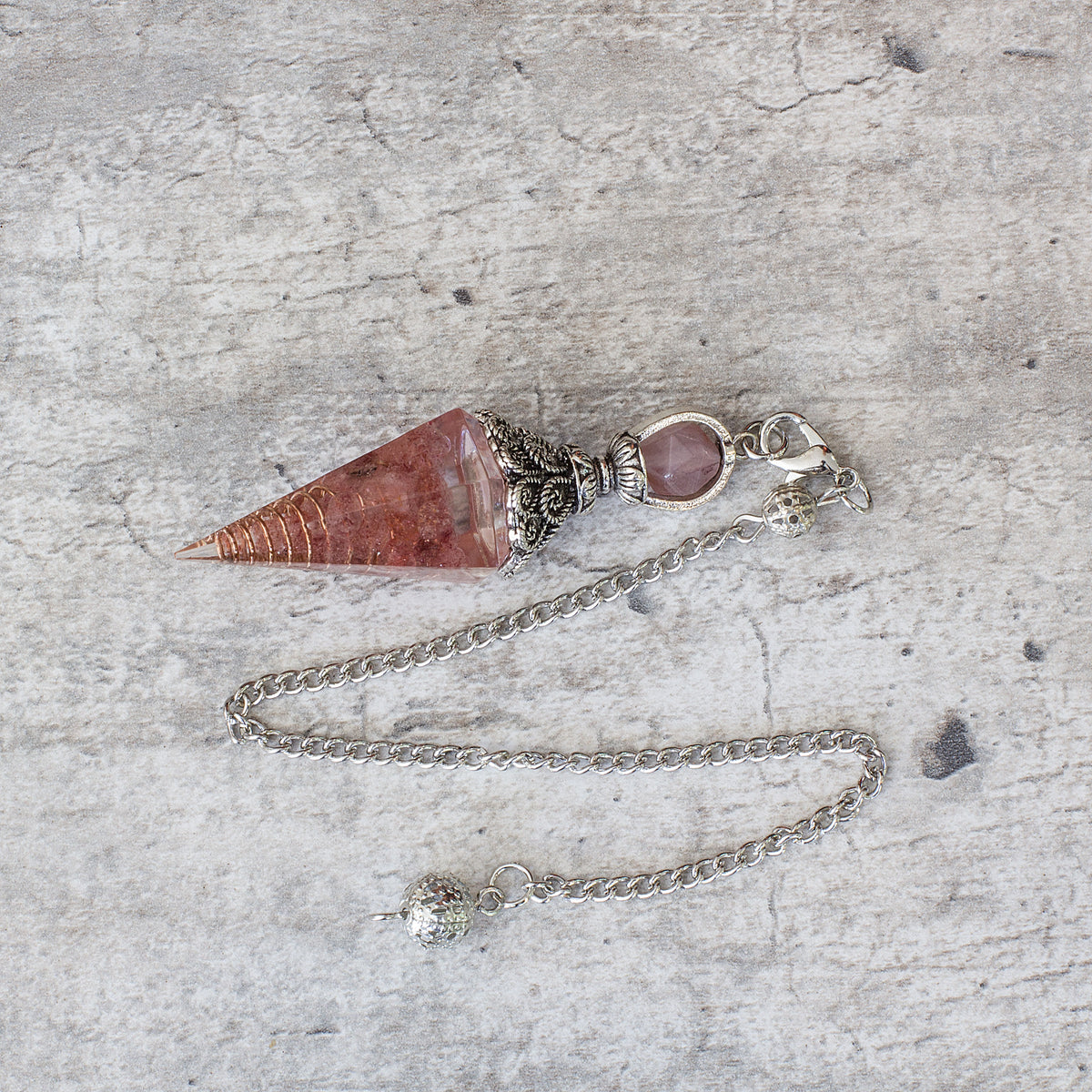 Pendulum - Strawberry Quartz - Resin Mi Chakra - A crystal pendulum is a simple tool commonly used for divination and dowsing. It typically consists of a crystal or gemstone suspended on a chain or cord. The crystal is usually pointed, allowing it to swing freely and respond to questions. Pendulums are believed to connect with your subconscious mind and energy fields, offering insights through their movements.