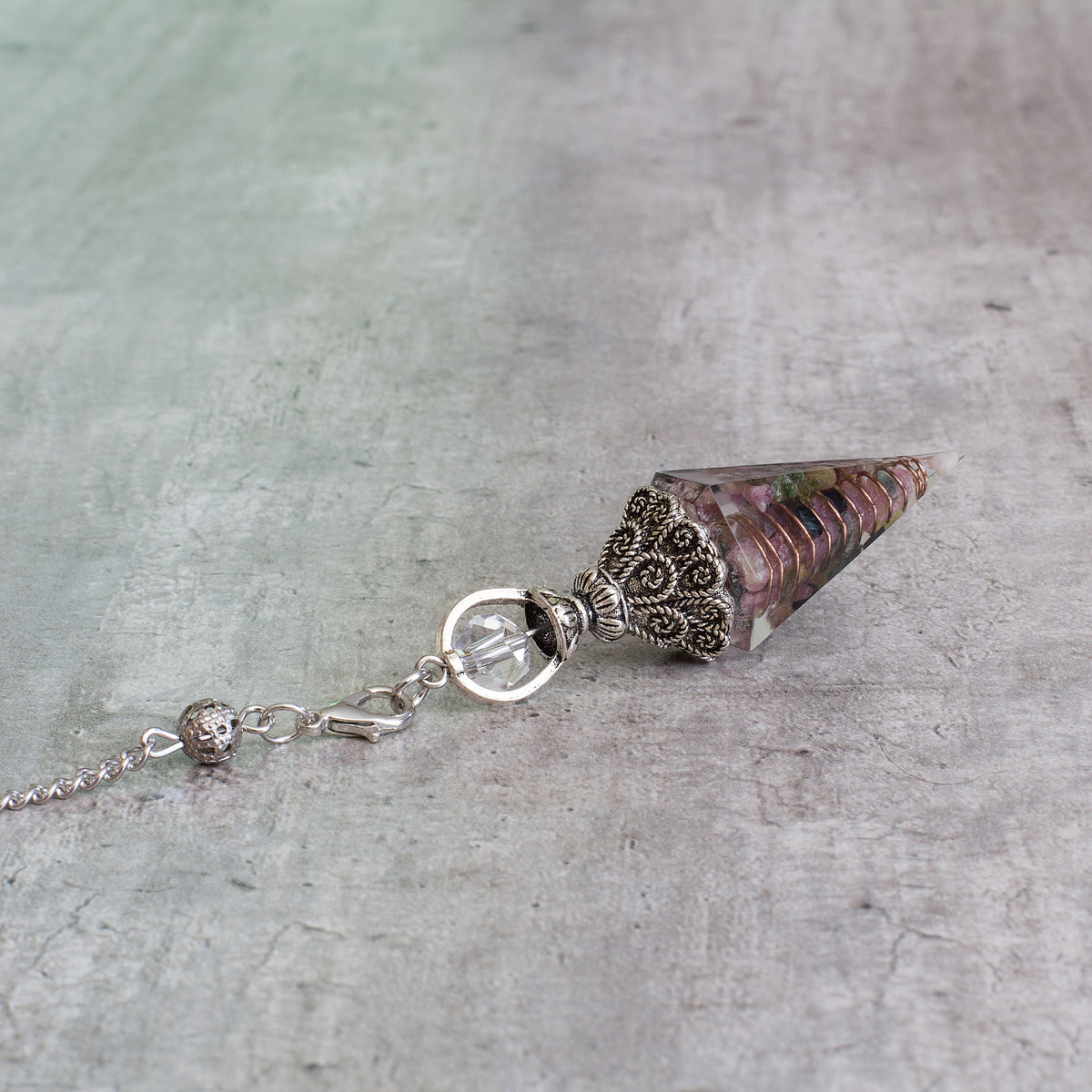 Pendulum - Tourmaline - Resin Mi Chakra - A crystal pendulum is a simple tool commonly used for divination and dowsing. It typically consists of a crystal or gemstone suspended on a chain or cord. The crystal is usually pointed, allowing it to swing freely and respond to questions. Pendulums are believed to connect with your subconscious mind and energy fields, offering insights through their movements.