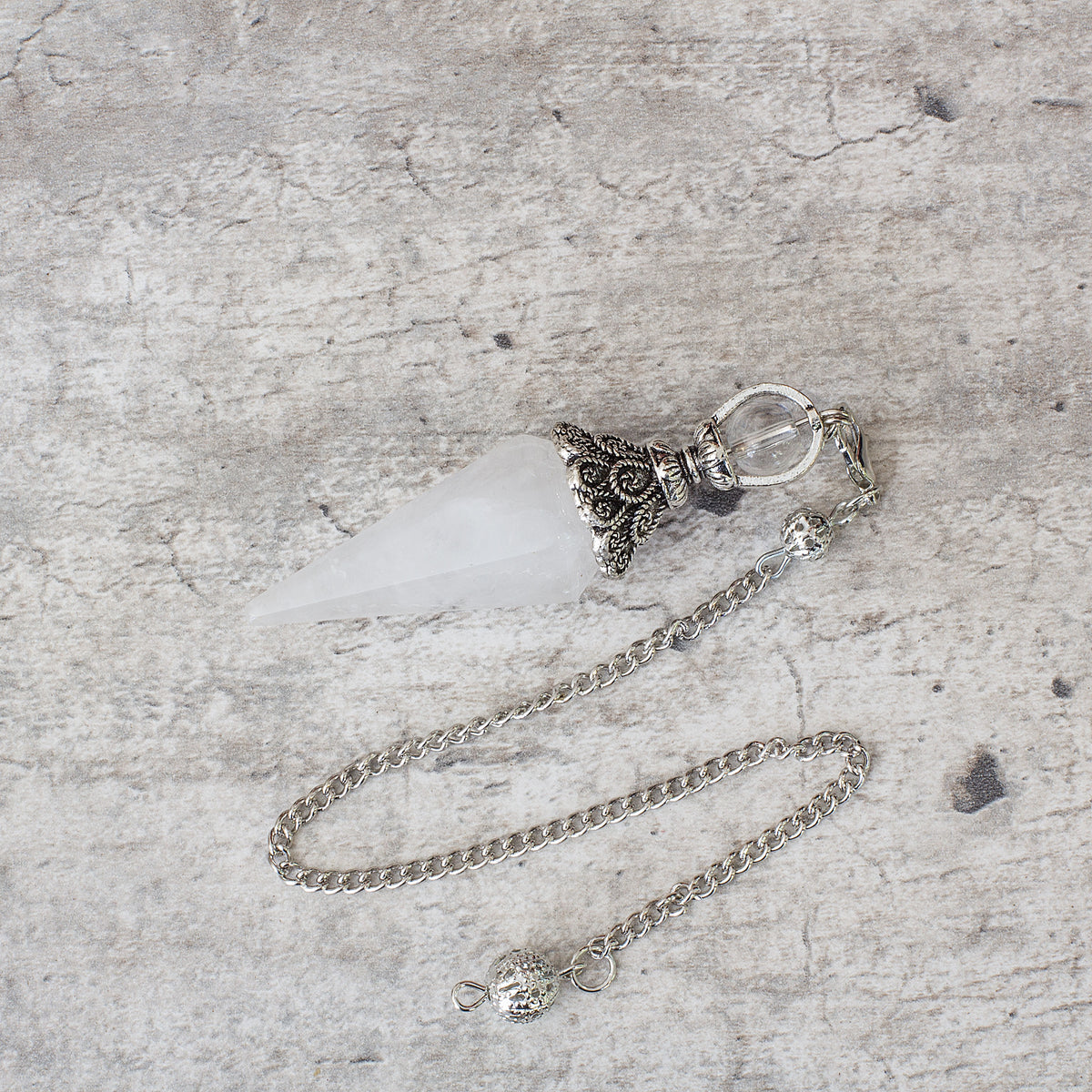Pendulum - Quartz Mi Chakra - A crystal pendulum is a simple tool commonly used for divination and dowsing. It typically consists of a crystal or gemstone suspended on a chain or cord. The crystal is usually pointed, allowing it to swing freely and respond to questions. Pendulums are believed to connect with your subconscious mind and energy fields, offering insights through their movements.