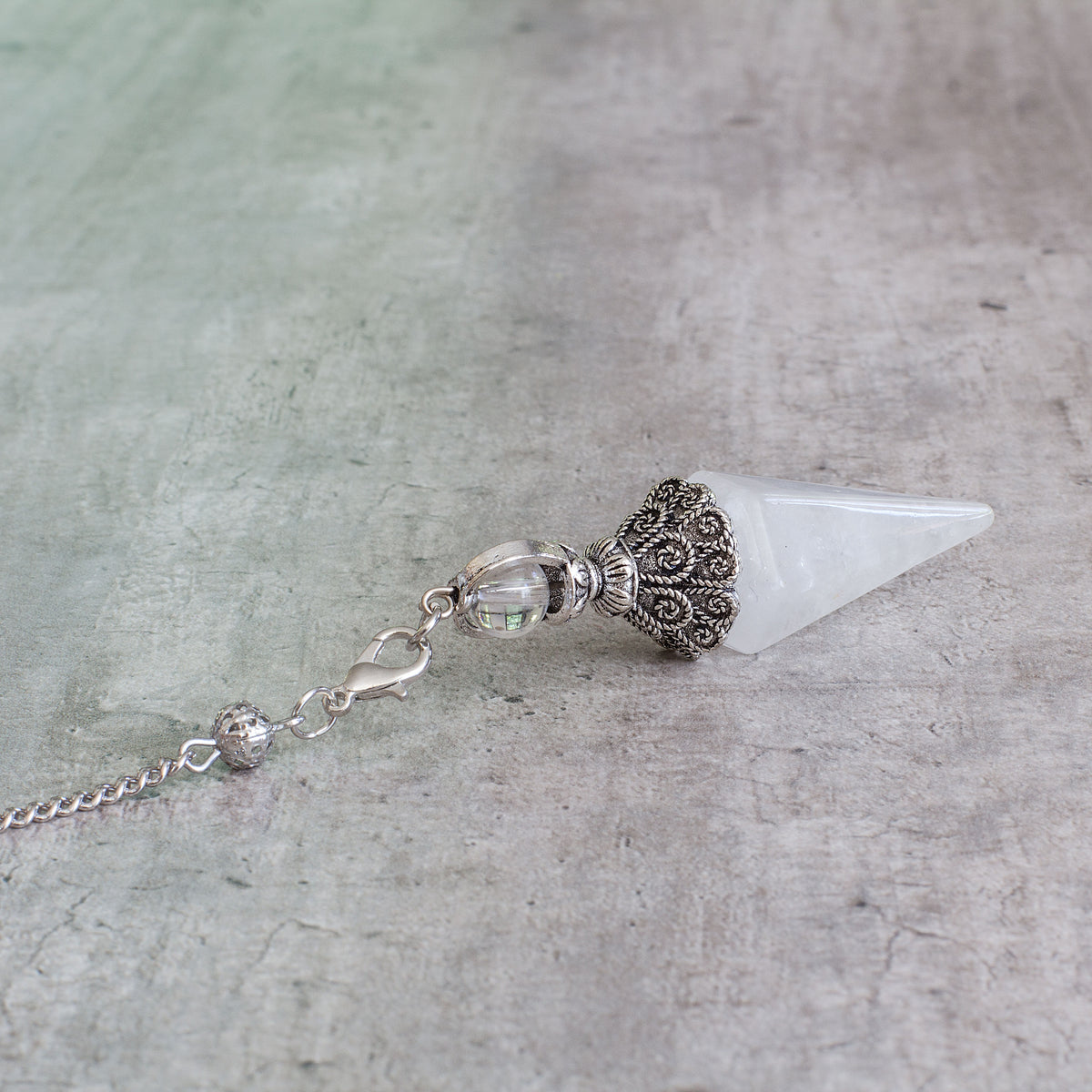 Pendulum - Quartz Mi Chakra - A crystal pendulum is a simple tool commonly used for divination and dowsing. It typically consists of a crystal or gemstone suspended on a chain or cord. The crystal is usually pointed, allowing it to swing freely and respond to questions. Pendulums are believed to connect with your subconscious mind and energy fields, offering insights through their movements.