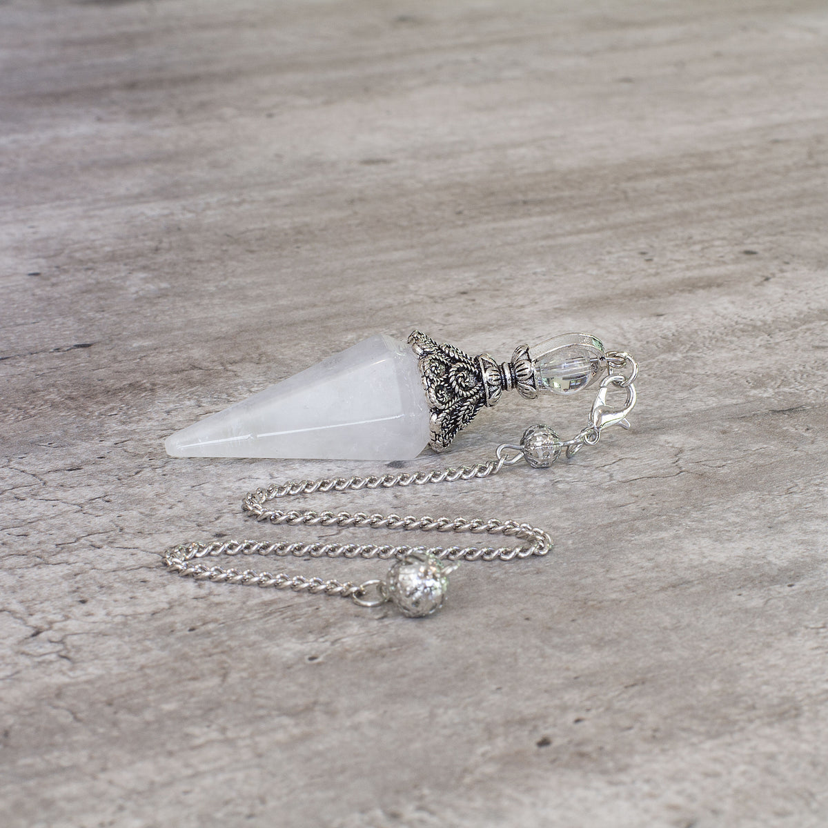 Pendulum - Quartz Mi Chakra - A crystal pendulum is a simple tool commonly used for divination and dowsing. It typically consists of a crystal or gemstone suspended on a chain or cord. The crystal is usually pointed, allowing it to swing freely and respond to questions. Pendulums are believed to connect with your subconscious mind and energy fields, offering insights through their movements.