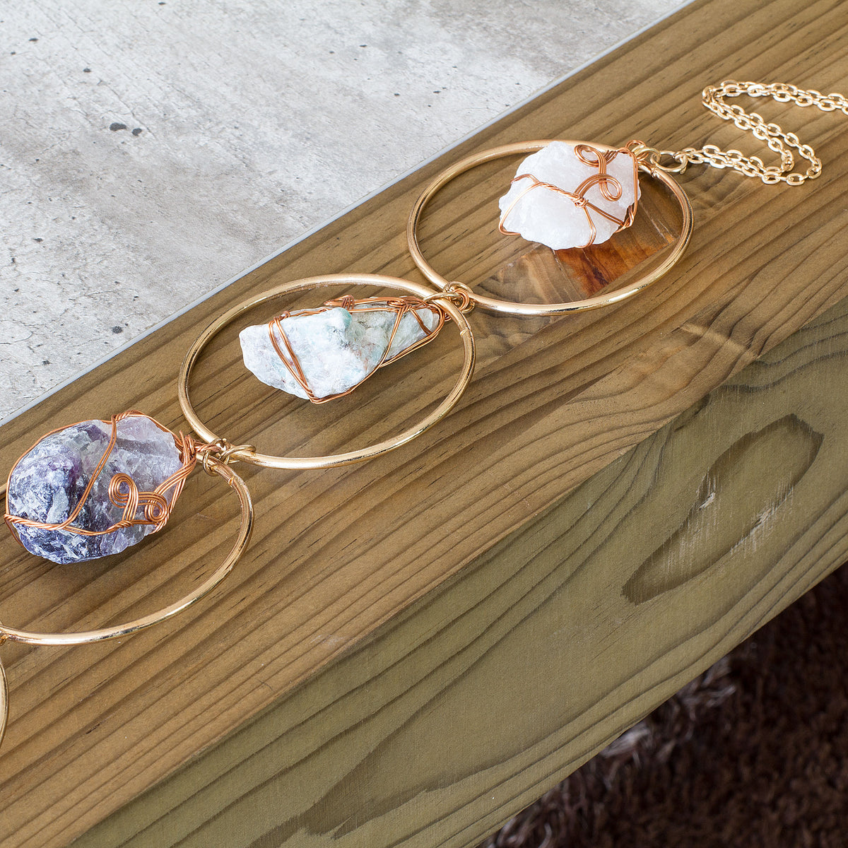 Turn your home into a haven of beauty and tranquility with this exceptional wall art meticulously handcrafted from genuine rough natural stones. Seven stunning, hand-selected chunks of Rose Quartz, Quartz Crystal, Green Aventurine, Amethyst, Fluorite, Amazonite, and Strawberry Quartz are carefully wrapped and suspended from an elegant, intricately detailed golden iron ring, creating a truly one-of-a-kind statement piece that will add an air of sophistication and natural charm to any room in your home.