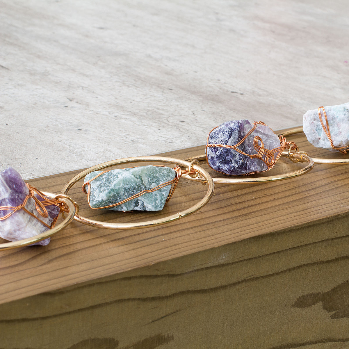 Turn your home into a haven of beauty and tranquility with this exceptional wall art meticulously handcrafted from genuine rough natural stones. Seven stunning, hand-selected chunks of Rose Quartz, Quartz Crystal, Green Aventurine, Amethyst, Fluorite, Amazonite, and Strawberry Quartz are carefully wrapped and suspended from an elegant, intricately detailed golden iron ring, creating a truly one-of-a-kind statement piece that will add an air of sophistication and natural charm to any room in your home.