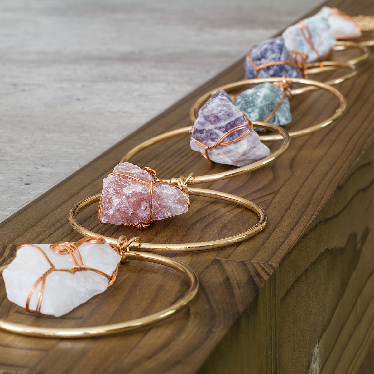 Turn your home into a haven of beauty and tranquility with this exceptional wall art meticulously handcrafted from genuine rough natural stones. Seven stunning, hand-selected chunks of Rose Quartz, Quartz Crystal, Green Aventurine, Amethyst, Fluorite, Amazonite, and Strawberry Quartz are carefully wrapped and suspended from an elegant, intricately detailed golden iron ring, creating a truly one-of-a-kind statement piece that will add an air of sophistication and natural charm to any room in your home.