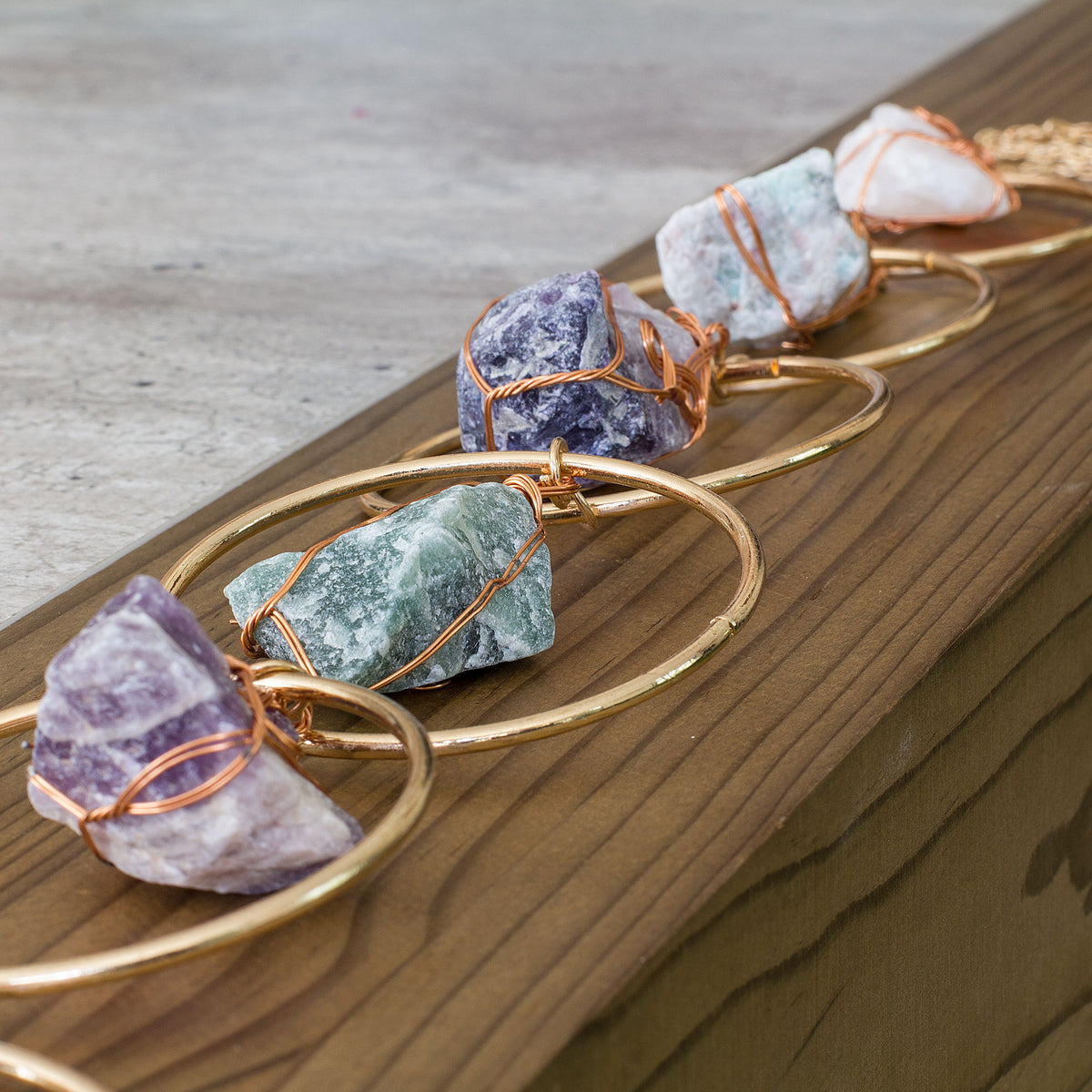Turn your home into a haven of beauty and tranquility with this exceptional wall art meticulously handcrafted from genuine rough natural stones. Seven stunning, hand-selected chunks of Rose Quartz, Quartz Crystal, Green Aventurine, Amethyst, Fluorite, Amazonite, and Strawberry Quartz are carefully wrapped and suspended from an elegant, intricately detailed golden iron ring, creating a truly one-of-a-kind statement piece that will add an air of sophistication and natural charm to any room in your home.